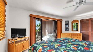 A bedroom with a bed, a TV on a wooden stand, a ceiling fan, and a view of the outside. - Lush View in Sunny Kona-Keauhou! Kitchen Ease, Lanai, Laundry, WiFi, TV Kanaloa 1204 (KAILUA-KONA)