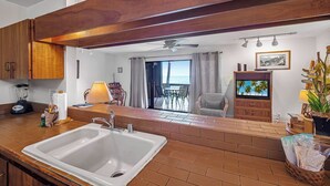 Una cocina con un lavamanos grande, armarios de madera, una licuadora y un comedor con una mesa y sillas.