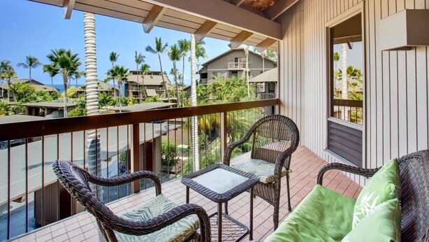Un balcón con mobiliario de mimbre y vistas a palmeras y casas.