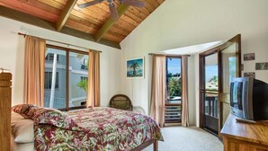 Un dormitorio con cama, techo de madera, televisor sobre un mueble de madera y vistas al exterior.
