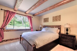 A bedroom with a wooden bed, a nightstand with a lamp, a window with curtains, and a view of greenery outside. - Lx18 golfers dream retreat for concours delegance (Pebble Beach)
