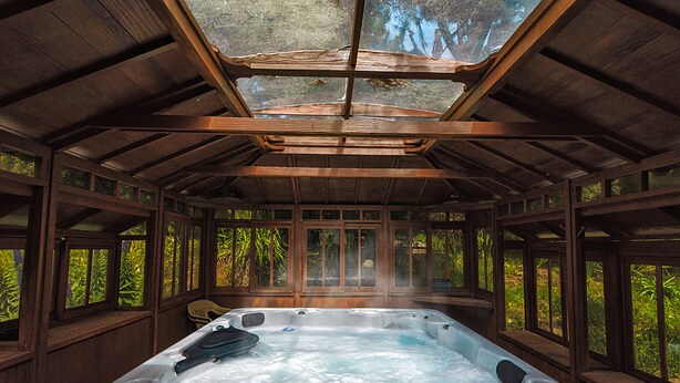 Un jacuzzi con techo de vidrio, rodeado de paredes y ventanas de madera.