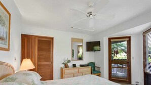 A bedroom with a bed, a ceiling fan, a television, a dresser, and a door with a view of the outdoors. - Tasteful Island Decor+Lanai w/Wet Bar, Full Kitchen, TV, WiFi, Washer/Dryer Kanaloa 301 (KAILUA-KONA)