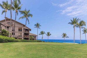 A multi-story hotel with balconies, a well-maintained lawn, and a view of the ocean. - Tasteful Island Decor+Lanai w/Wet Bar, Full Kitchen, TV, WiFi, Washer/Dryer Kanaloa 301 (KAILUA-KONA)