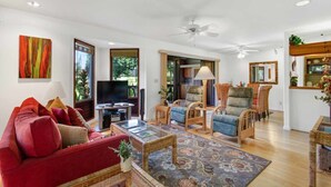 A spacious living room with a red sofa, wicker furniture, a flat-screen TV, and a ceiling fan. - Tasteful Island Decor+Lanai w/Wet Bar, Full Kitchen, TV, WiFi, Washer/Dryer Kanaloa 301 (KAILUA-KONA)