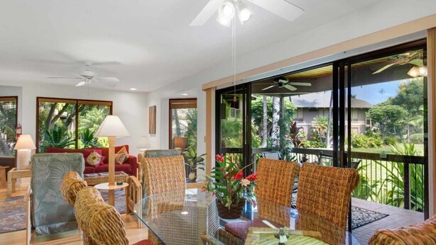 A spacious living area with a glass dining table, wicker chairs, and a ceiling fan. - Tasteful Island Decor+Lanai w/Wet Bar, Full Kitchen, TV, WiFi, Washer/Dryer Kanaloa 301 (KAILUA-KONA)