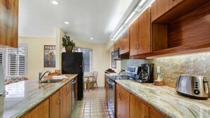 Una cocina con armarios de madera, encimera de granito, refrigerador, microondas, tostadora y un lavabo.