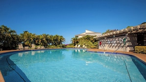 A clear blue pool with lounge chairs and palm trees.