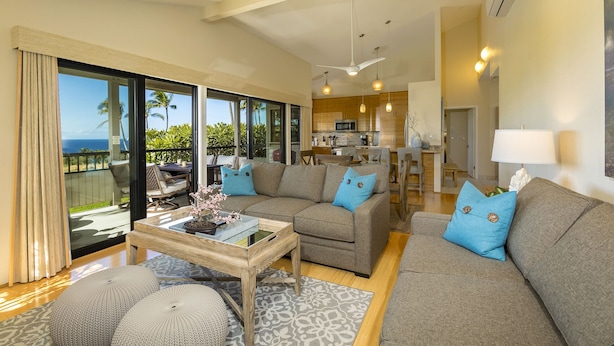 A modern living room with a large sofa, a coffee table, and a view of the ocean through large sliding doors.