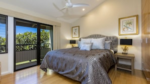 A bedroom with a large bed, a ceiling fan, a balcony with plants, and artwork on the walls.