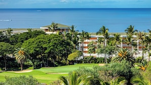 A golf course with a view of the ocean and a hotel with multiple floors and palm trees.