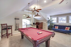 A pool table in a room with a ceiling fan, a blue sofa, and a potted plant.