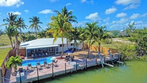 A house with a pool, surrounded by palm trees, and a dock extending into a body of water. - P43 - Spacious 3 bedroom 3 bath home with Pool in the Sombrero Beach Area (Marathon)