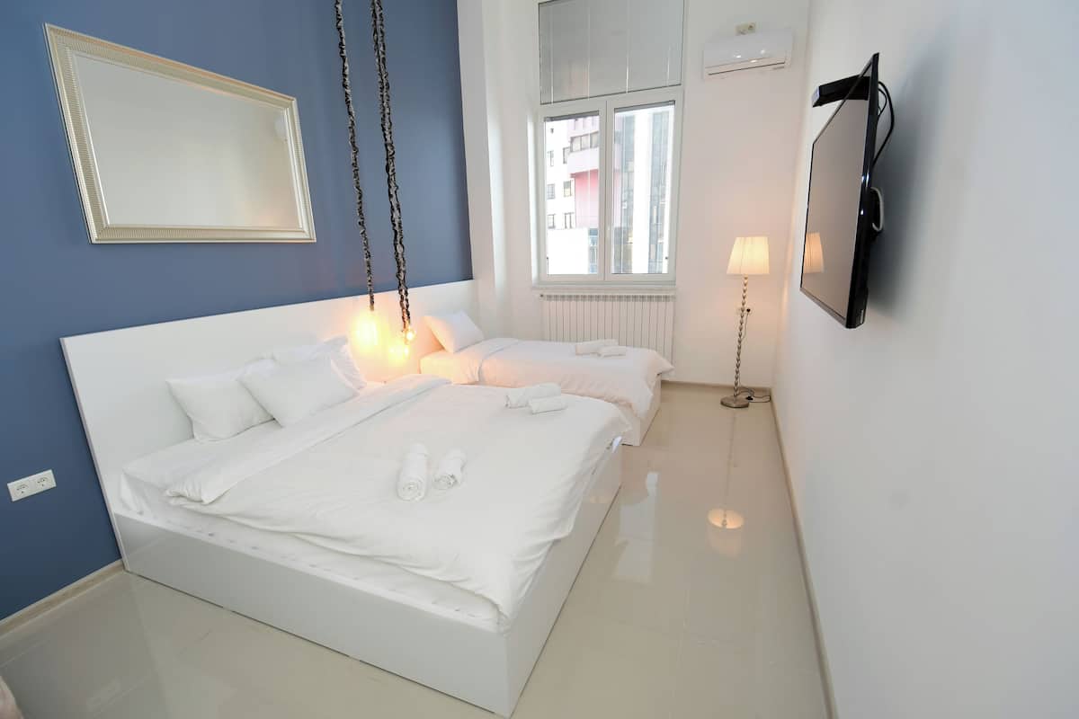 A hotel room with a large bed, a TV, a window, and a lamp.