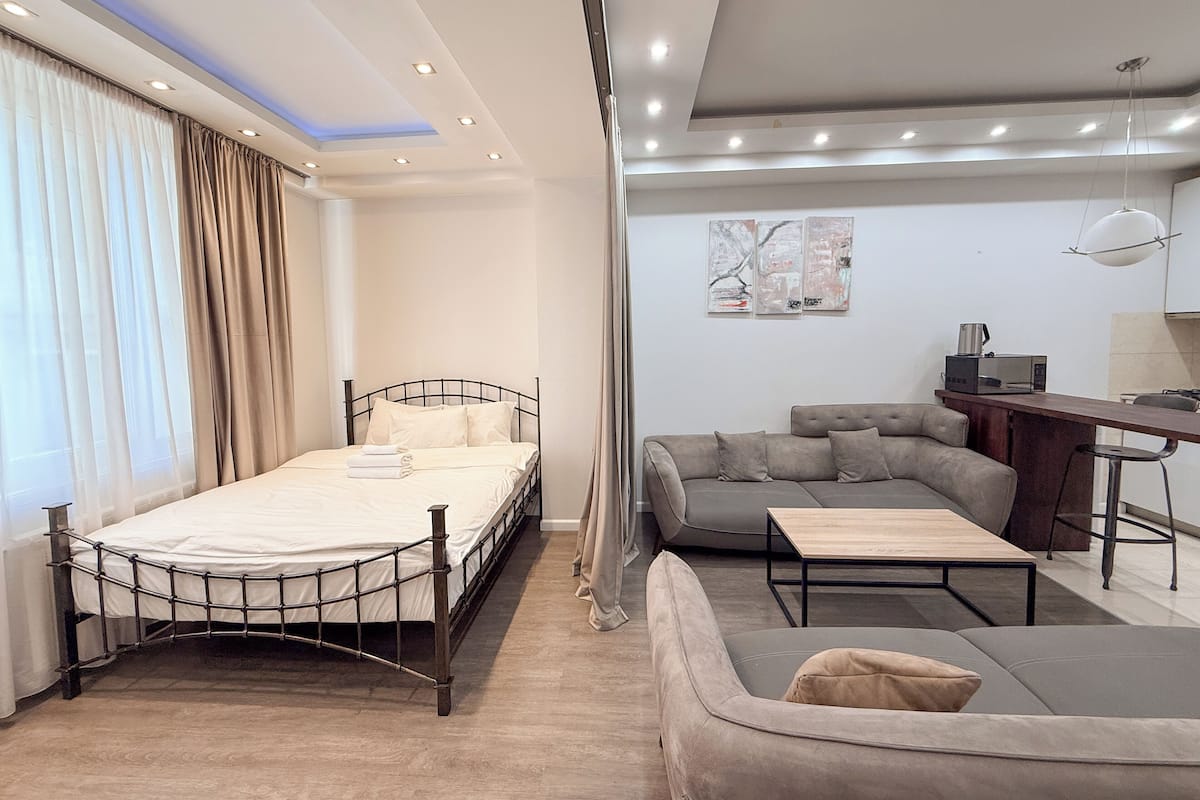 A modern hotel room with a bed, sofa, and a small dining area.