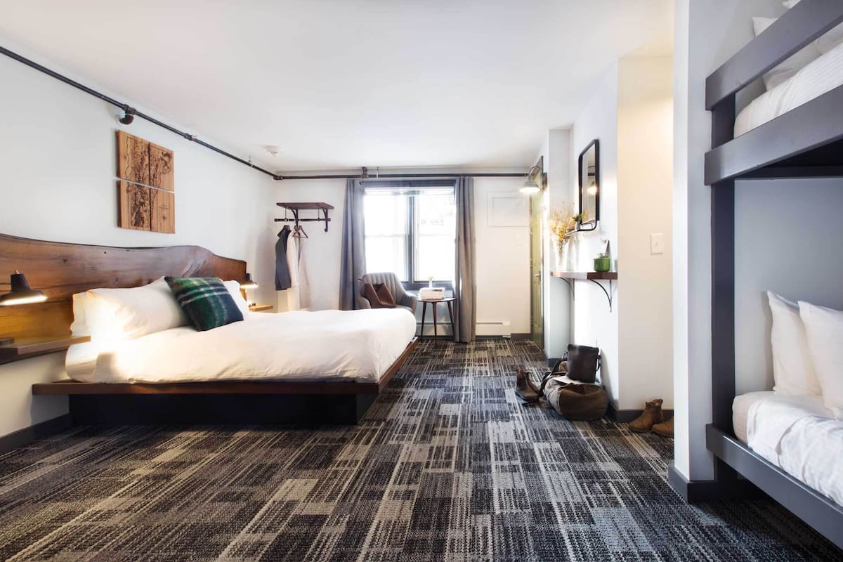 A modern hotel room with a large bed, a desk, and a bunk bed.