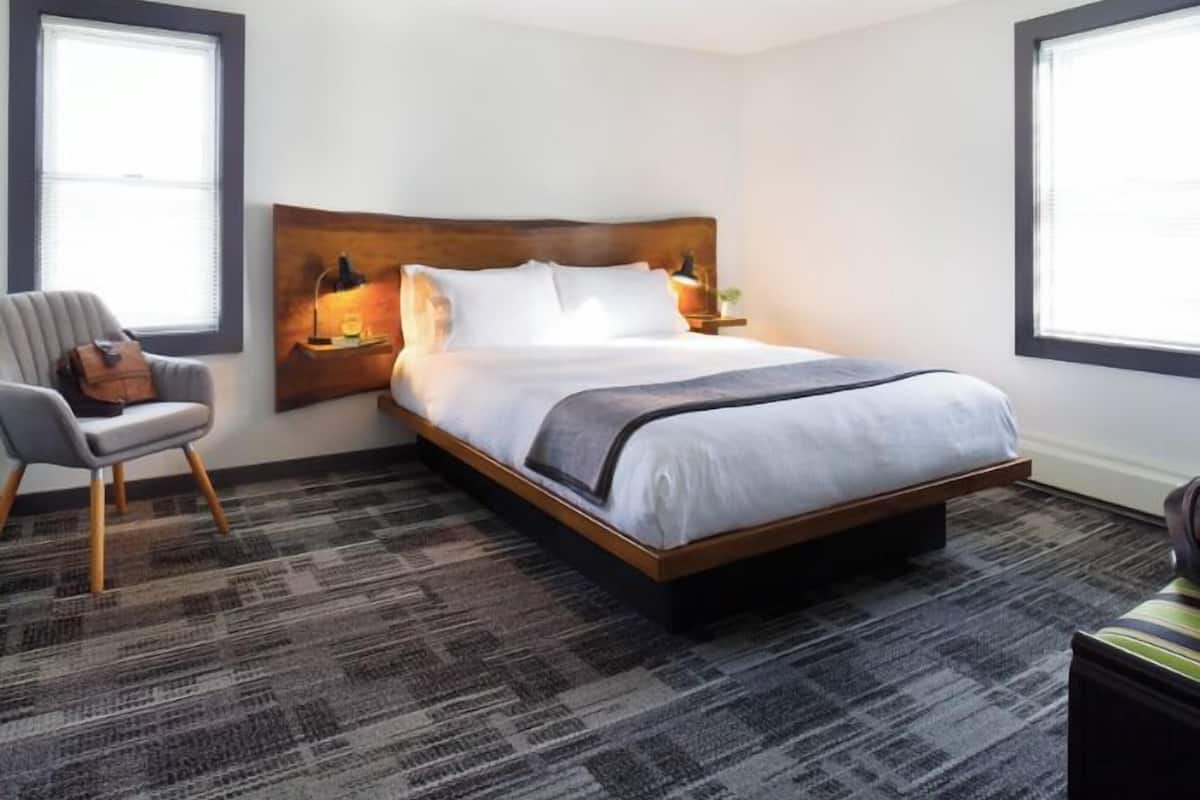 A hotel room with a large bed, a chair, and a nightstand with a lamp.