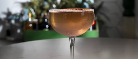 A cocktail glass on a marble countertop with a hexagonal wall pattern and a sign reading "MAIN + MOUNTAIN".