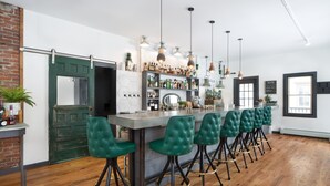 A bar area with a long counter, green upholstered bar stools, and a variety of bottles and glasses on shelves. - Main and Mountain Bar & Motel (Ludlow)