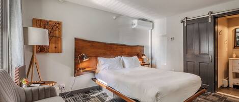 A modern bedroom with a wooden headboard, a single bed, a desk with a lamp, and a view of a sliding door.