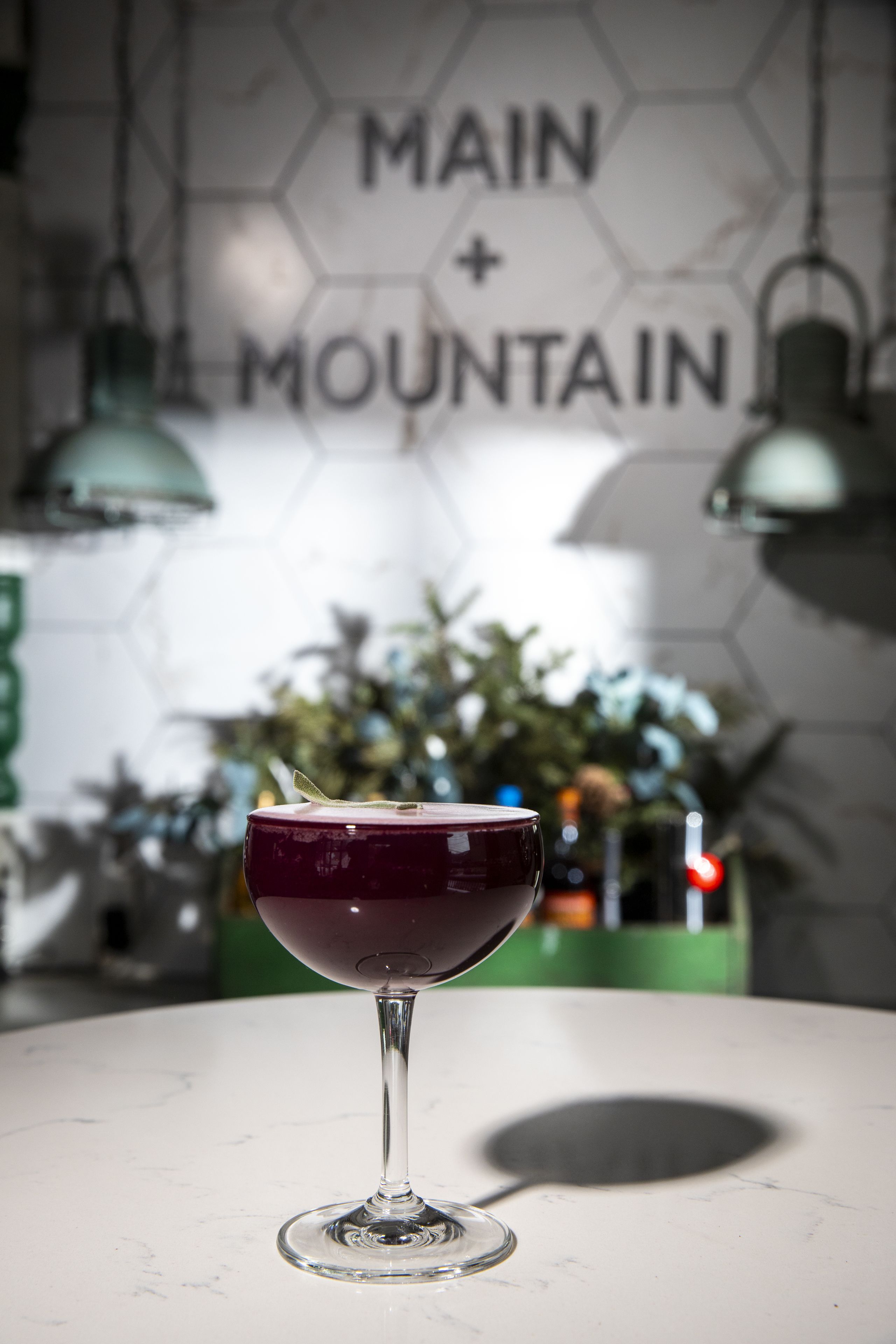 A glass of red wine on a white table with a hexagonal wall pattern and hanging lights in the background.