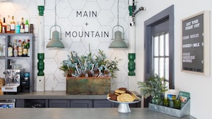 A bar area with a hexagonal tiled wall, a wooden planter with greenery, a metal tray with cookies, and a menu board on the wall. - Main and Mountain Bar & Motel (Ludlow)