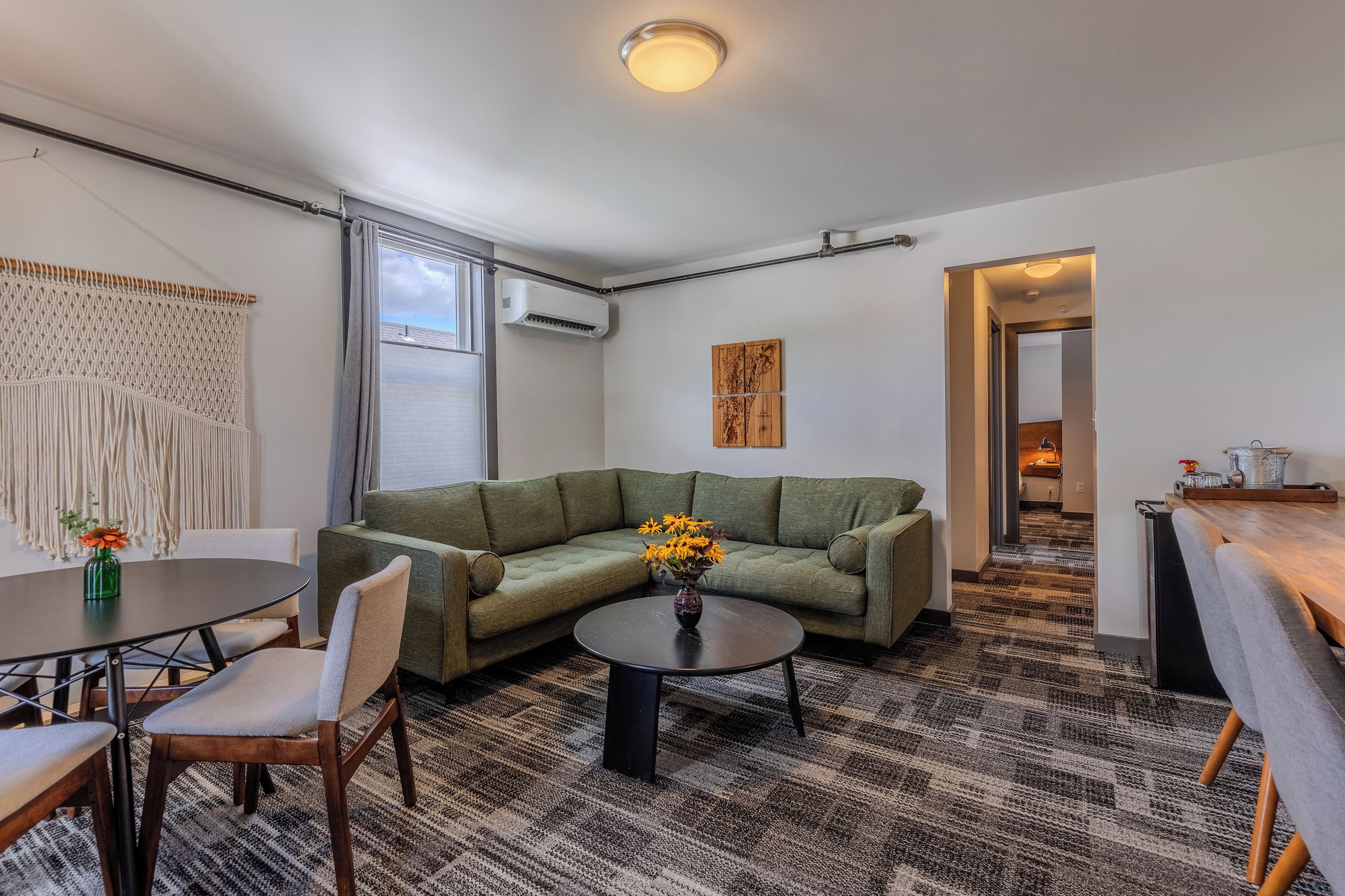 A modern living room with a green sofa, a round coffee table, and a dining area with a table and chairs.
