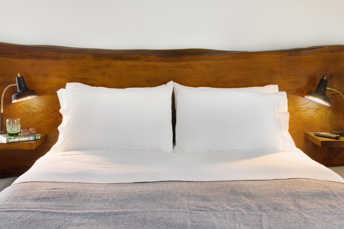 A neatly made bed with white linens, a wooden headboard, and two bedside tables with lamps and a remote control.