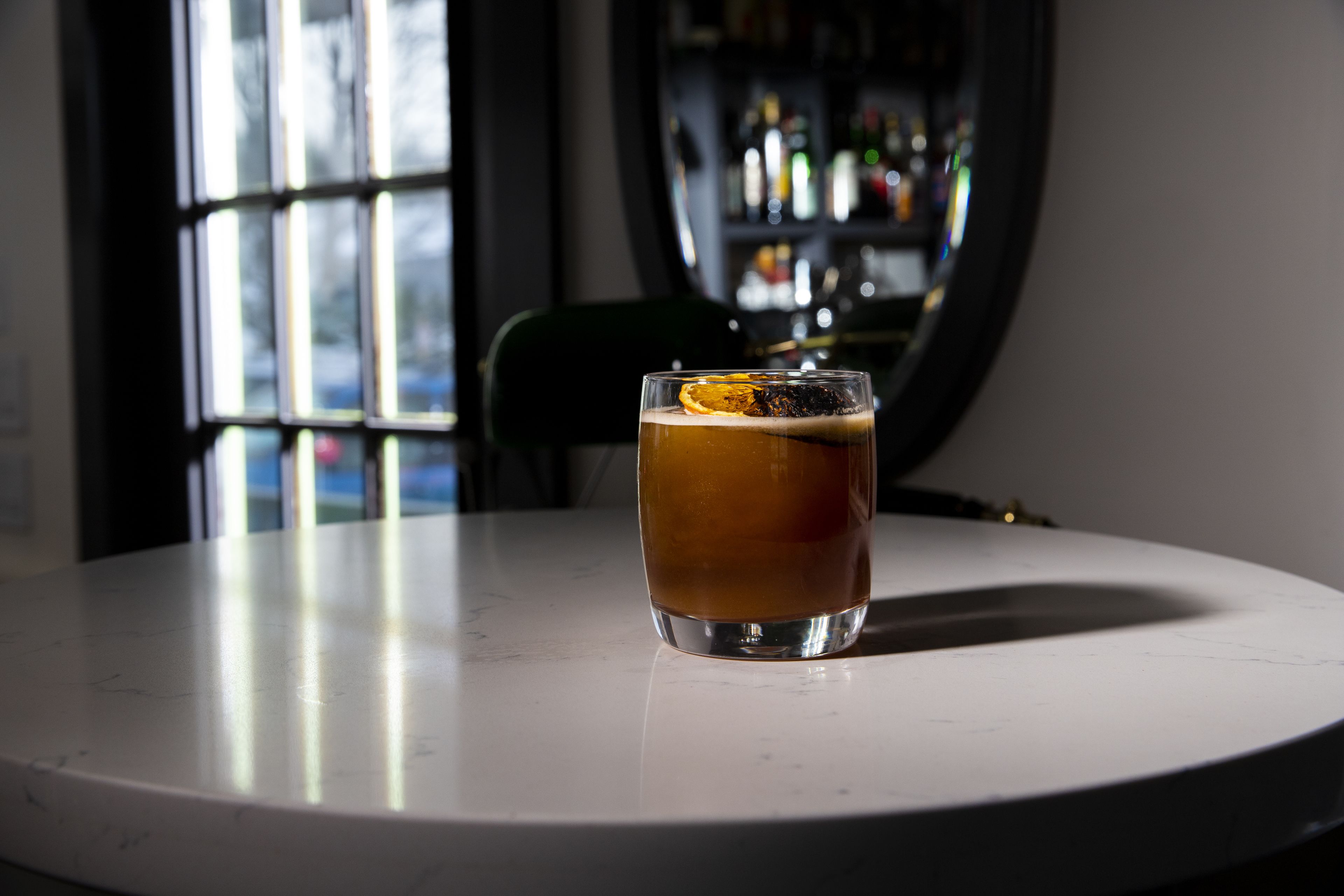 Un verre de bière sur une table blanche, avec une fenêtre en arrière-plan.