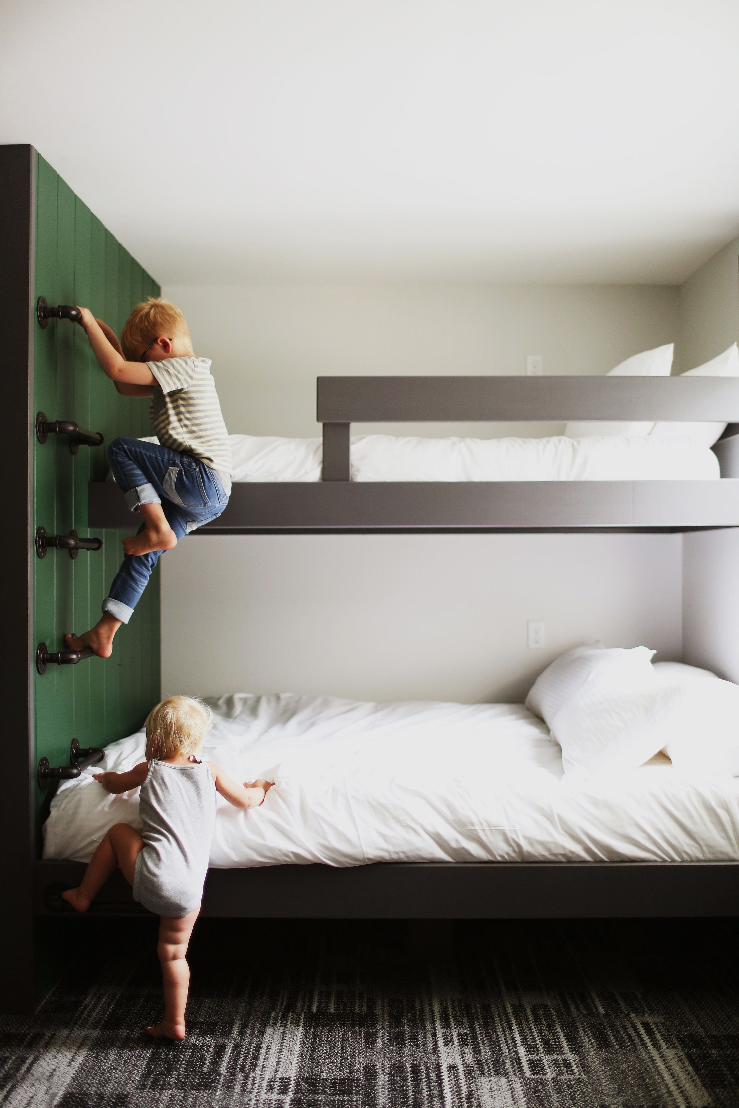 A bunk bed with a child climbing the wall and another child on the lower bunk.
