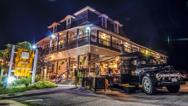 A two-story building with a bar and restaurant on the ground floor, a vintage car parked in front, and a sign indicating "Main Mountain". - Main and Mountain Bar & Motel (Ludlow)