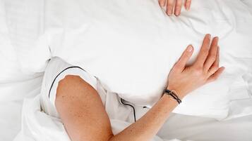 A person lying in bed with white bedding, wearing a white shirt with black trim.