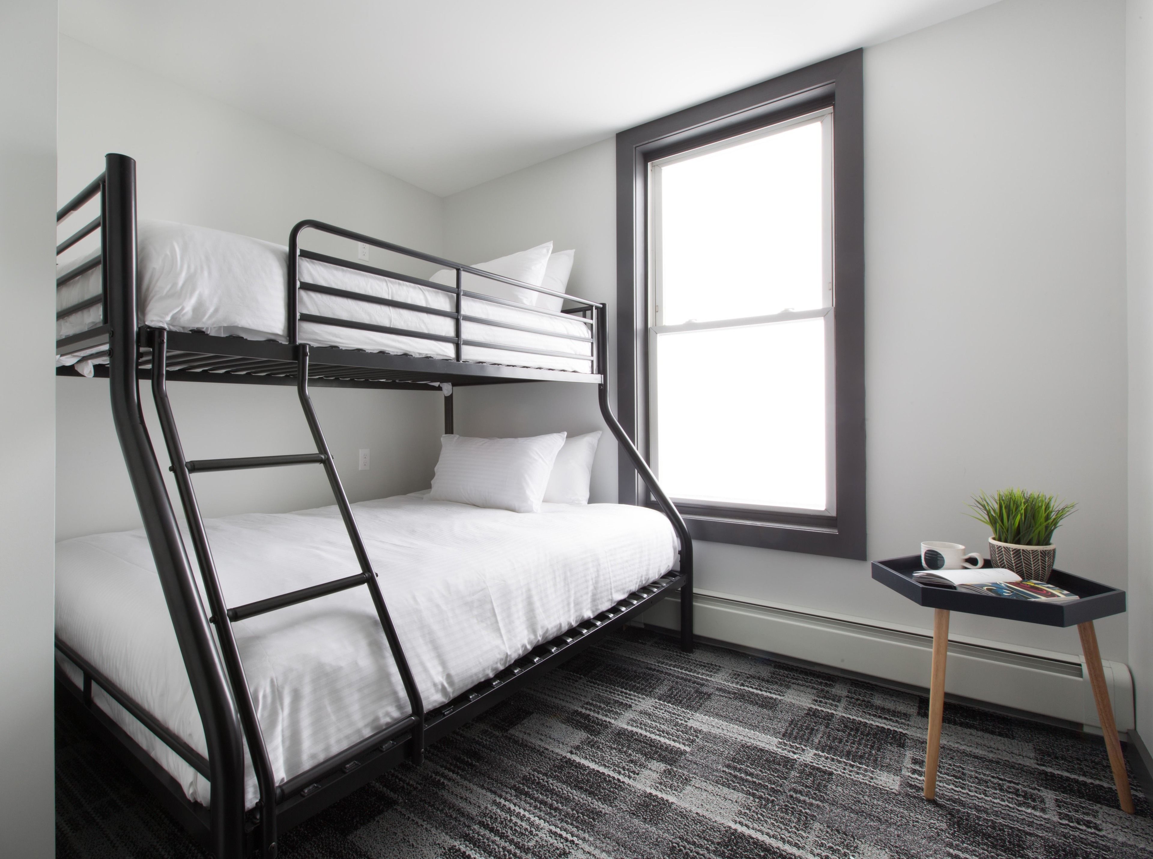 A bunk bed room with a window, a small table with a plant, and a radiator.