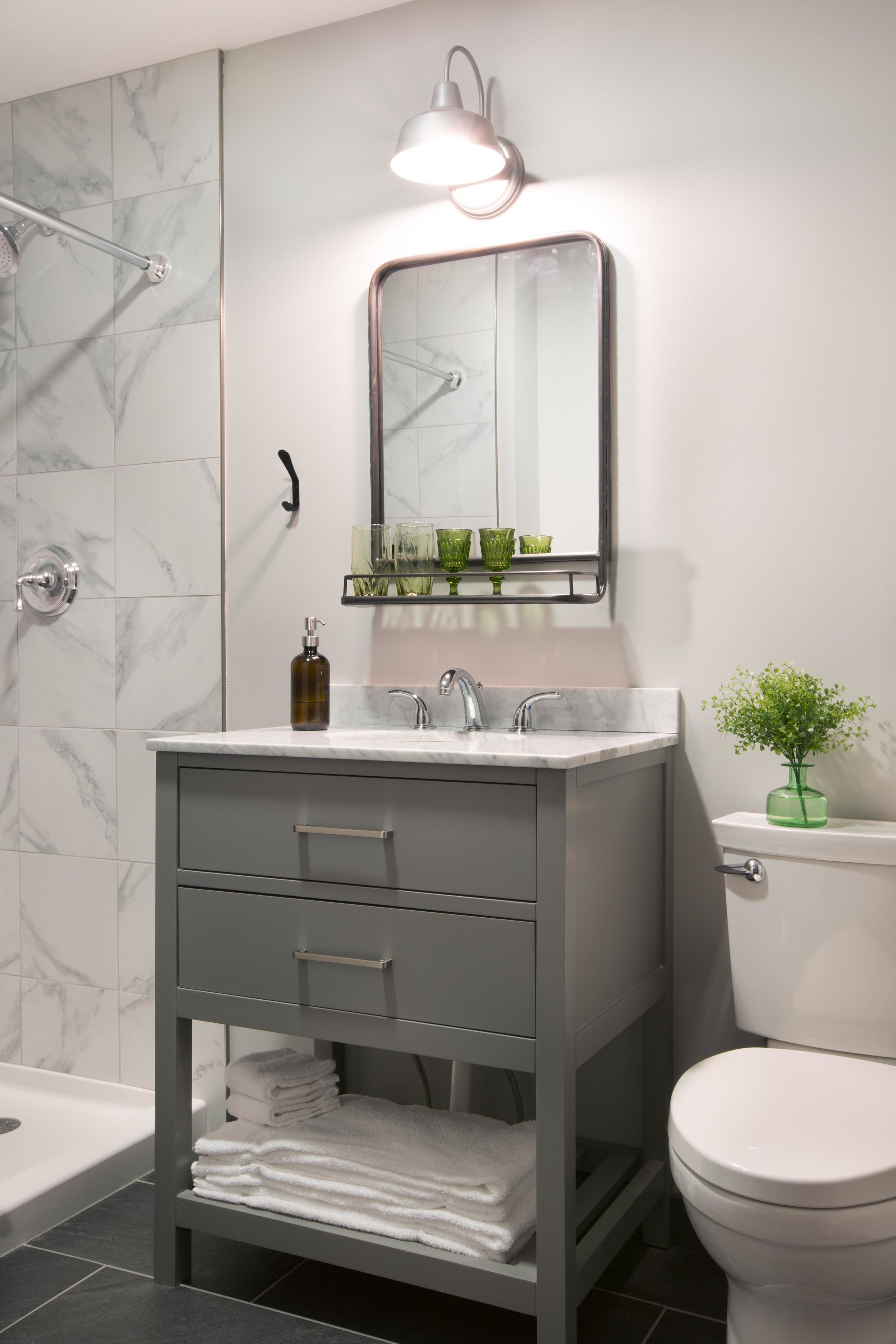 A modern bathroom with a marble shower, a vanity with a mirror, and a toilet.