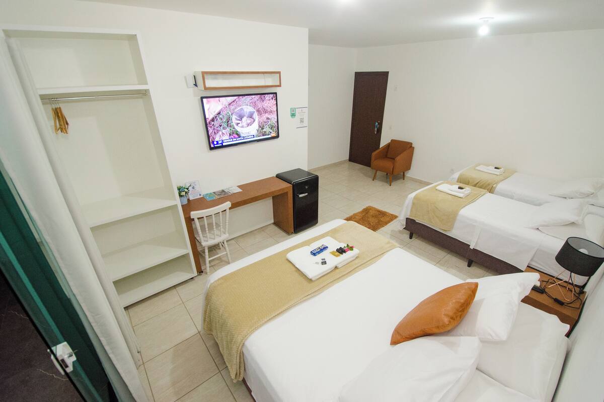 Quarto de hotel com duas camas, uma escrivaninha, uma televisão e um guarda-roupa.