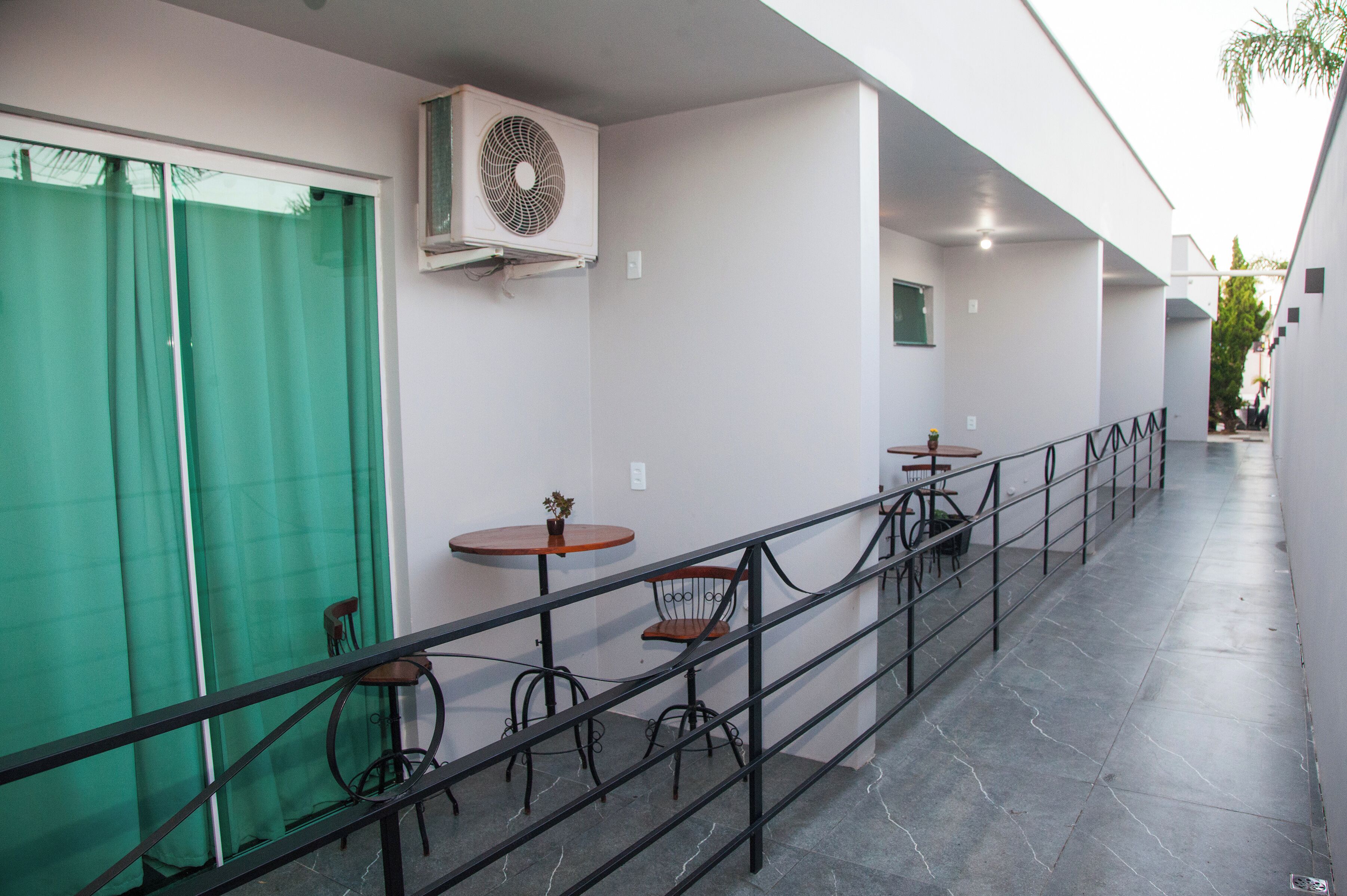 A covered outdoor seating area with tables and chairs, a green curtain, and an air conditioning unit.
