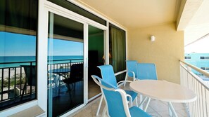 Un balcon avec une table et des chaises, une vue sur l’océan et un bâtiment en arrière-plan.