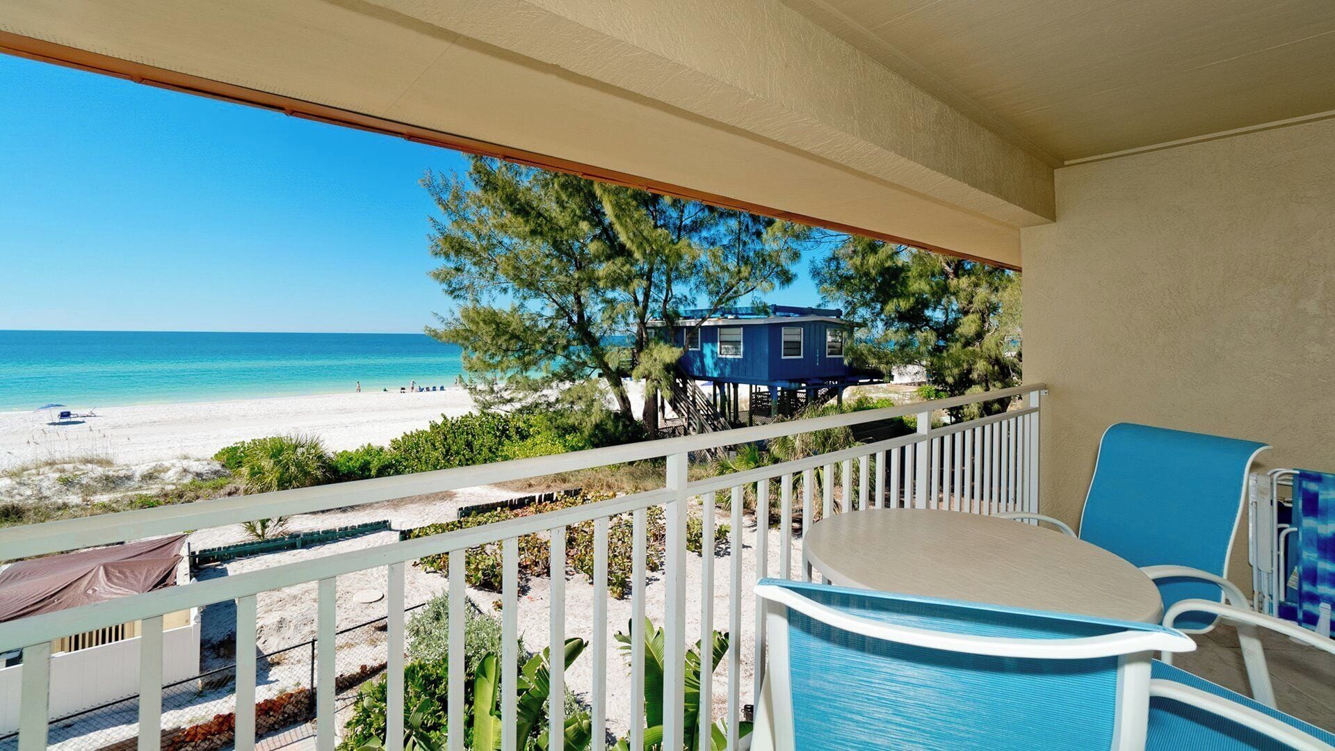 A balcony with a view of a beach and ocean, featuring a small table and chairs.