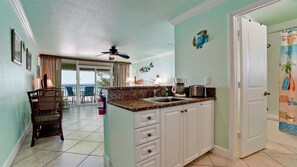 A kitchen with a view to the outside, a ceiling fan, and a door with a beach-themed curtain.