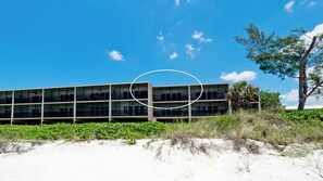 A modern building with multiple floors and large windows, situated on a sandy beach with greenery and a clear blue sky. - Sunset Terrace 203  - Anna Maria Island - Beach front condo 2 Bedroom/ 2 Bath Bradenton Beach, Anna Maria Island, maximum occupancy of 4 people. (Bradenton Beach)