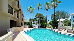 A swimming pool surrounded by palm trees and a building with balconies.