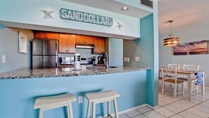 Una cucina con una parete blu a contrasto, mobili in legno, elettrodomestici in acciaio inossidabile e un'area bar con due sgabelli.