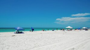 A beach with white sand and clear blue water. There are several umbrellas and tents set up for shade. - Sunset Terrace 203  - Anna Maria Island - Beach front condo 2 Bedroom/ 2 Bath Bradenton Beach, Anna Maria Island, maximum occupancy of 4 people. (Bradenton Beach)