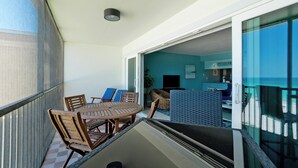 Un balcón con una mesa y sillas, una puerta corrediza de vidrio que da a una habitación con un televisor y un letrero que dice "SANDDOLLAR".