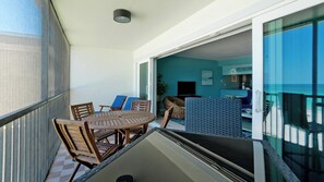A balcony with a table and chairs, a sliding glass door leading to a room with a TV and a sign reading "SANDDOLLAR".