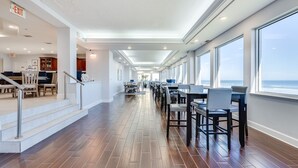 Un vaste couloir doté d’un plancher en bois, d’un escalier et d’un coin repas avec des tables et des chaises.