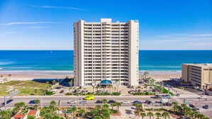 Un hôtel de grande hauteur, avec de nombreux étages, une vue sur la plage et un parking où sont garées des voitures.