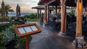 An outdoor seating area with a wet floor sign, wooden pillars, and a view of the ocean.