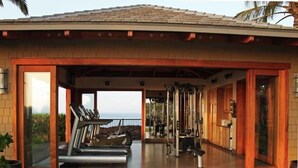 A covered outdoor gym with exercise equipment, a view of the ocean, and a patio area.