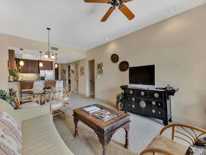 A spacious living area with a sofa, coffee table, and dining set. A TV is mounted on the wall, and there is a ceiling fan. - Ground Floor 2 Bedroom-Halii Kai at Waikoloa 18C (WAIKOLOA)